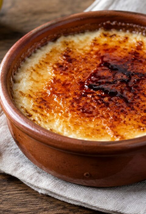 Cazuelita de barro con arroz con leche asturiano cremoso y costra de azúcar requemado, junto a una rama de canela y piel de limón